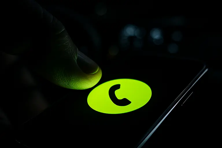 Thumb about to tap a glowing lime call button on a phone at night